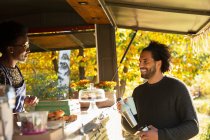 Cliente feliz hablando con el propietario del carrito de comida en el parque de otoño - foto de stock