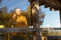 Mann telefoniert am sonnigen Restaurantfenster mit Smartphone — Stockfoto