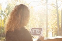 Frau chattet mit Freunden auf digitalem Tablet am sonnigen Fenster — Stockfoto