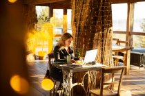 Empresária trabalhando no laptop no café ensolarado — Fotografia de Stock