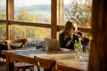 Бізнес-леді розмовляє по телефону в ноутбуці в сонячному ресторані — стокове фото