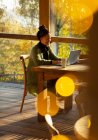 Propriétaire de petite entreprise travaillant à l'ordinateur portable dans un café d'automne ensoleillé — Photo de stock