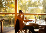 Бизнесмен с наушниками работает за ноутбуком в солнечном осеннем кафе — стоковое фото
