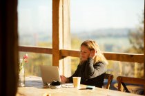 Бізнес-леді працює за ноутбуком за сонячним столом кафе — стокове фото