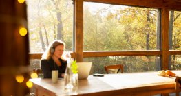 Geschäftsfrau mit Kopfhörer arbeitet im sonnigen Herbstcafé am Laptop — Stockfoto