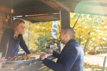 Happy friendly food cart owner talking with customer in autumn park — Stock Photo