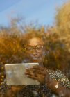 Femme souriante utilisant une tablette numérique à la fenêtre ensoleillée d'automne — Photo de stock