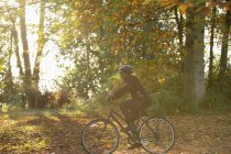 Mujer feliz bicicleta entre las hojas de otoño en el parque soleado - foto de stock