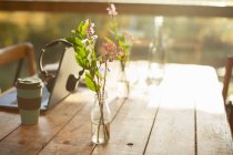 Arranjo de flores silvestres simples em garrafa de vidro na mesa de café rústica — Fotografia de Stock