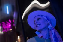 Mulher na moda feliz em fedora sob luzes de néon — Fotografia de Stock