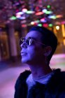 Portrait stylish young man in sunglasses looking up at neon lights — Stock Photo