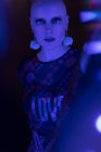 Retrato mujer seria con la cabeza afeitada en luz azul neón oscuro - foto de stock