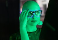 Retrato mulher elegante com cabeça raspada em óculos de néon em luz verde — Fotografia de Stock
