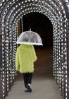 Giovane eccentrico in cappotto di piuma con ombrello sotto luci ad arco — Foto stock