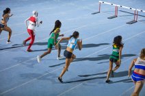 Female track and field athletes running hurdle race on blue track — Stock Photo