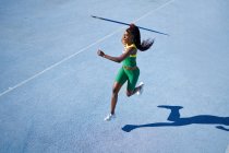 Female track and field athlete throwing javelin on sunny blue track — Stock Photo