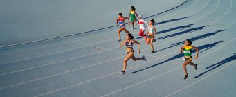 Atletas de pista e campo do sexo feminino correndo em corrida em pista azul — Fotografia de Stock
