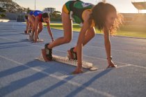 Atletas de atletismo do sexo feminino em blocos iniciais em pista ensolarada — Fotografia de Stock