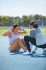 Female track and field athletes doing sit ups on sunny track — Stock Photo
