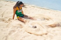 Atletismo feminino e atleta de campo saltando para a areia — Fotografia de Stock