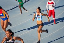 Female track and field athletes running in competition on sunny track — Stock Photo