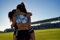 Happy female track and field athletes hugging in stadium infield — Stock Photo