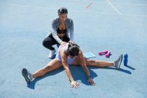 Trainer helping female track and female athlete stretch on track — Stock Photo