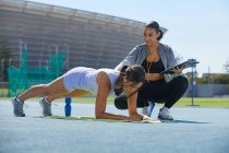 Trainer helping female track and field athlete doing planks on track — Stock Photo