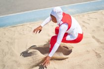 Female track and field athlete in hijab long jumping in sand — Stock Photo
