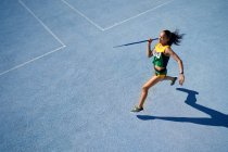 Female track and field athlete throwing javelin on sunny blue track — Stock Photo