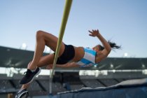 Female track and field athlete high jumping over pole — Stock Photo
