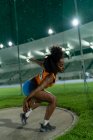Female track and field athlete throwing discus in stadium at night — Stock Photo
