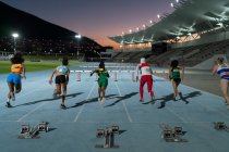 Female track and field athletes racing to hurdles on track at night — Stock Photo