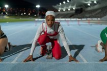 Retrato determinado corredor femenino en hijab en la línea de salida de la pista - foto de stock
