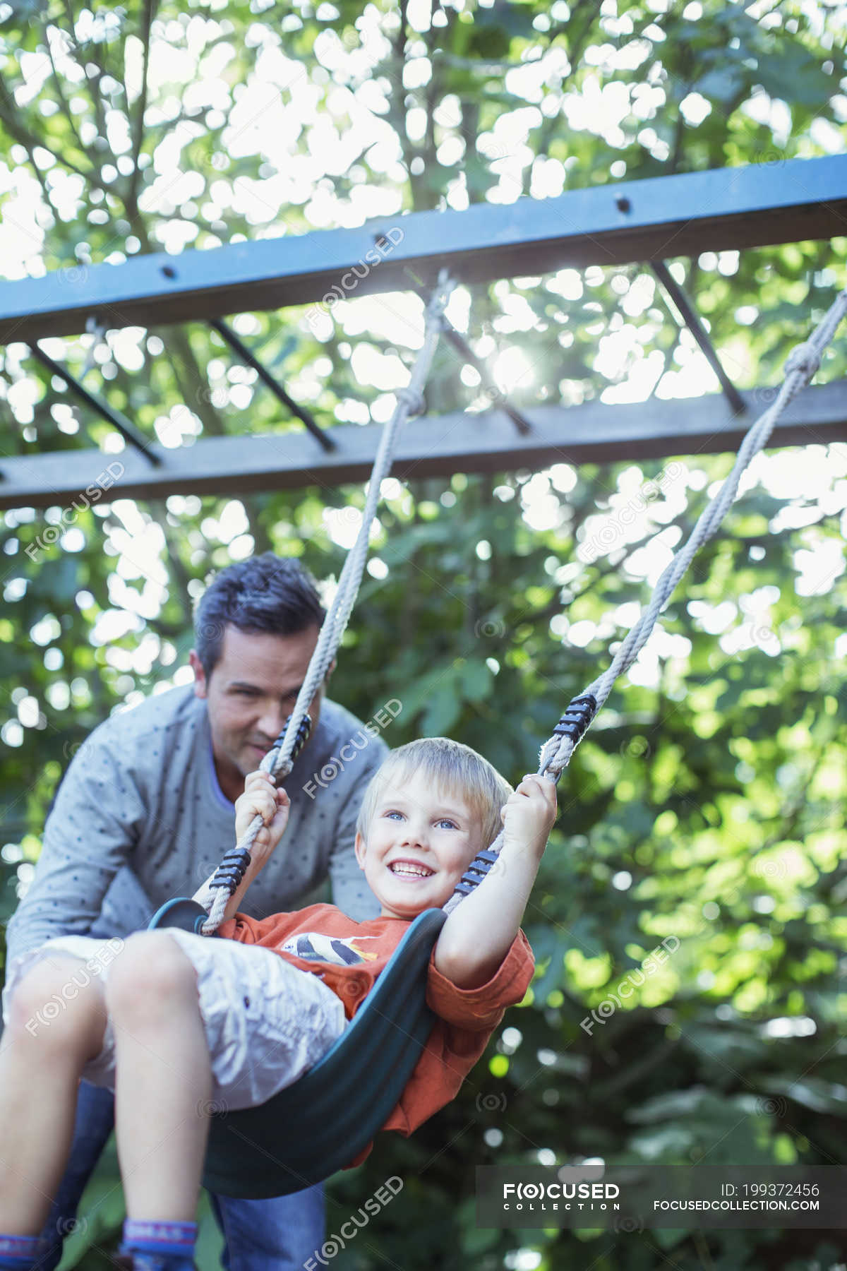 Father Pushing Son On Swing Outdoors Toothy Smile Two