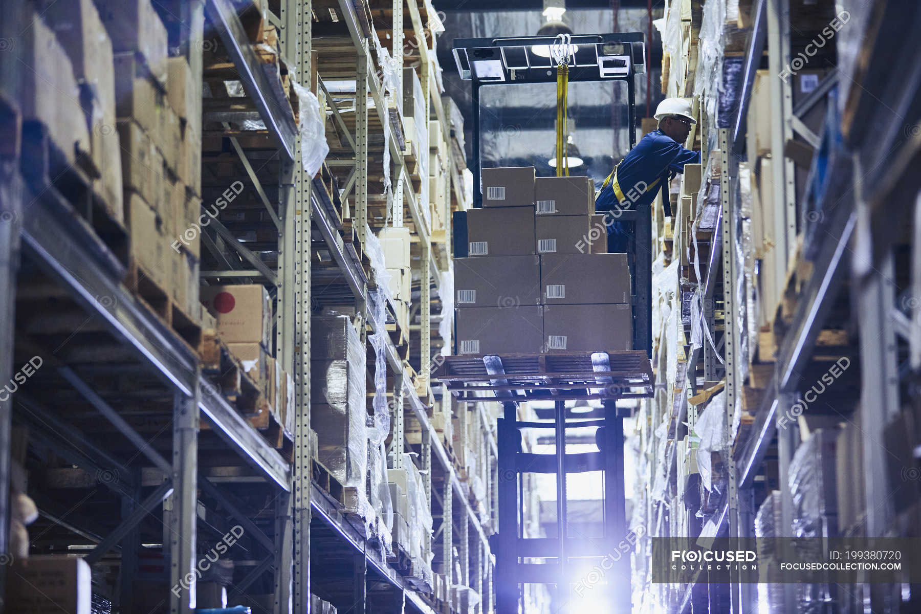 Worker operating forklift stacking cardboard boxes on distribution