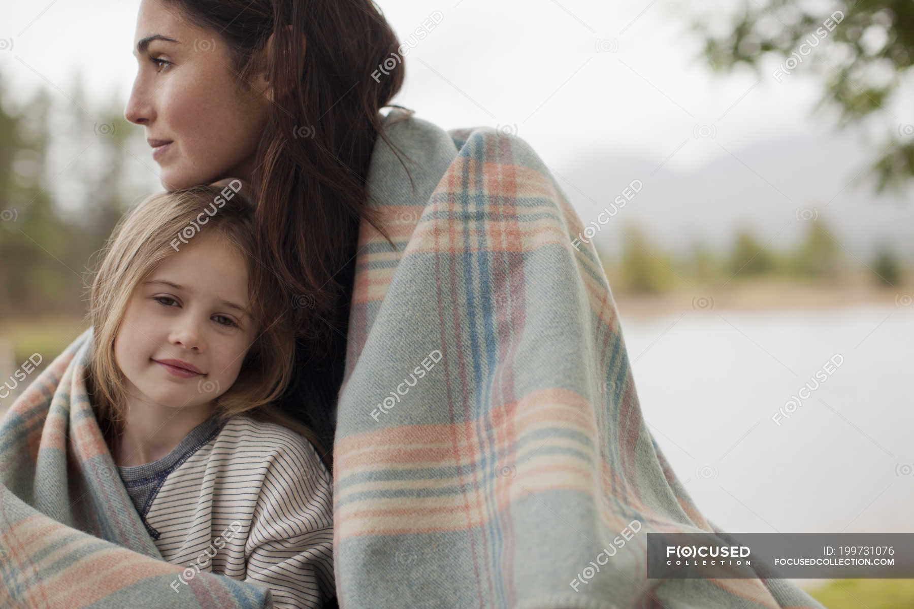 Portrait of smiling daughter wrapped in blanket with mother at lakeside — happiness, long hair