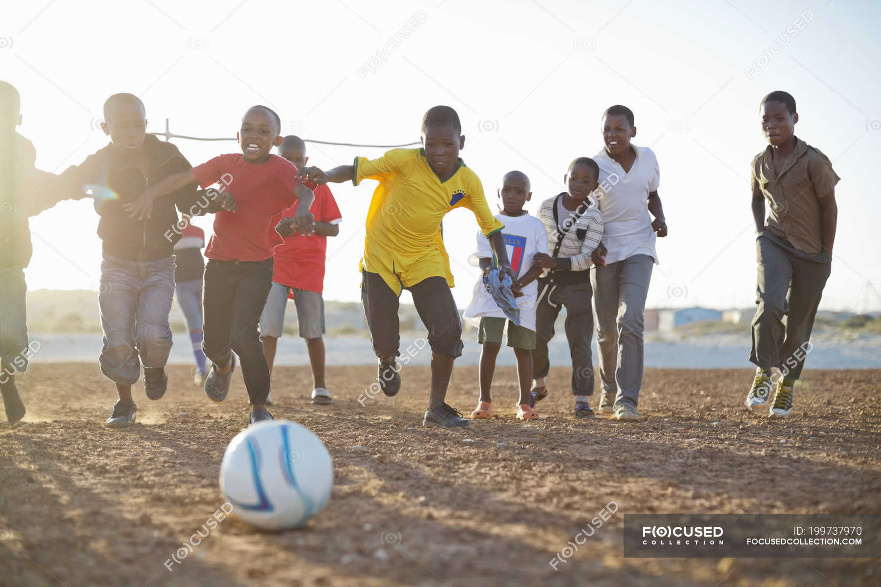 African playing soccer together in dirt field — teamwork, Casual Clothing - Photo | #199737970