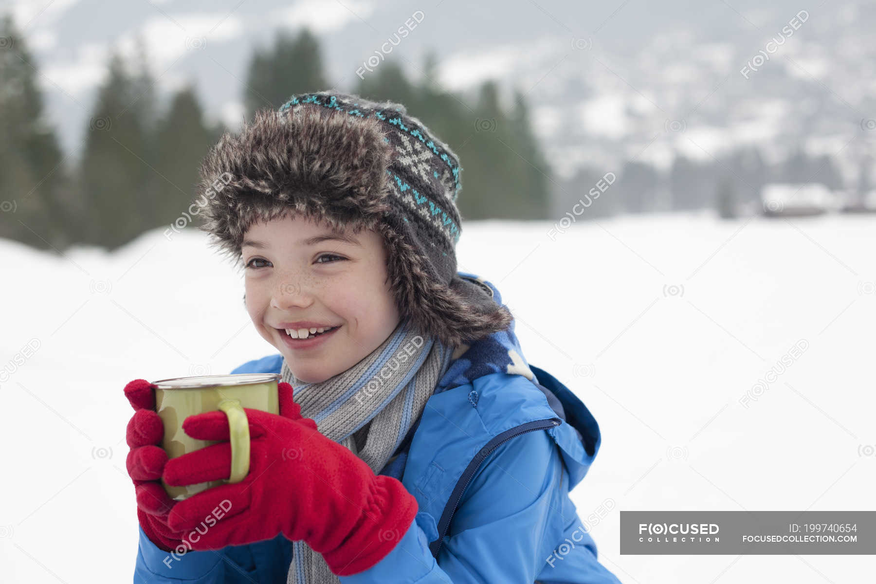 happy-boy-drinking-hot-chocolate-in-snowy-field-holding-winter