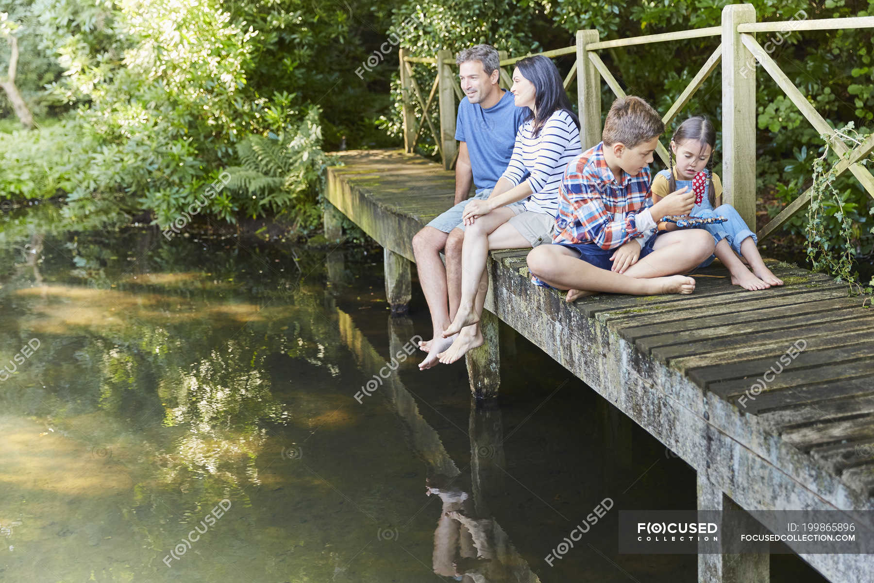 family-relaxing-on-footbridge-over-pond-connection-travel-stock