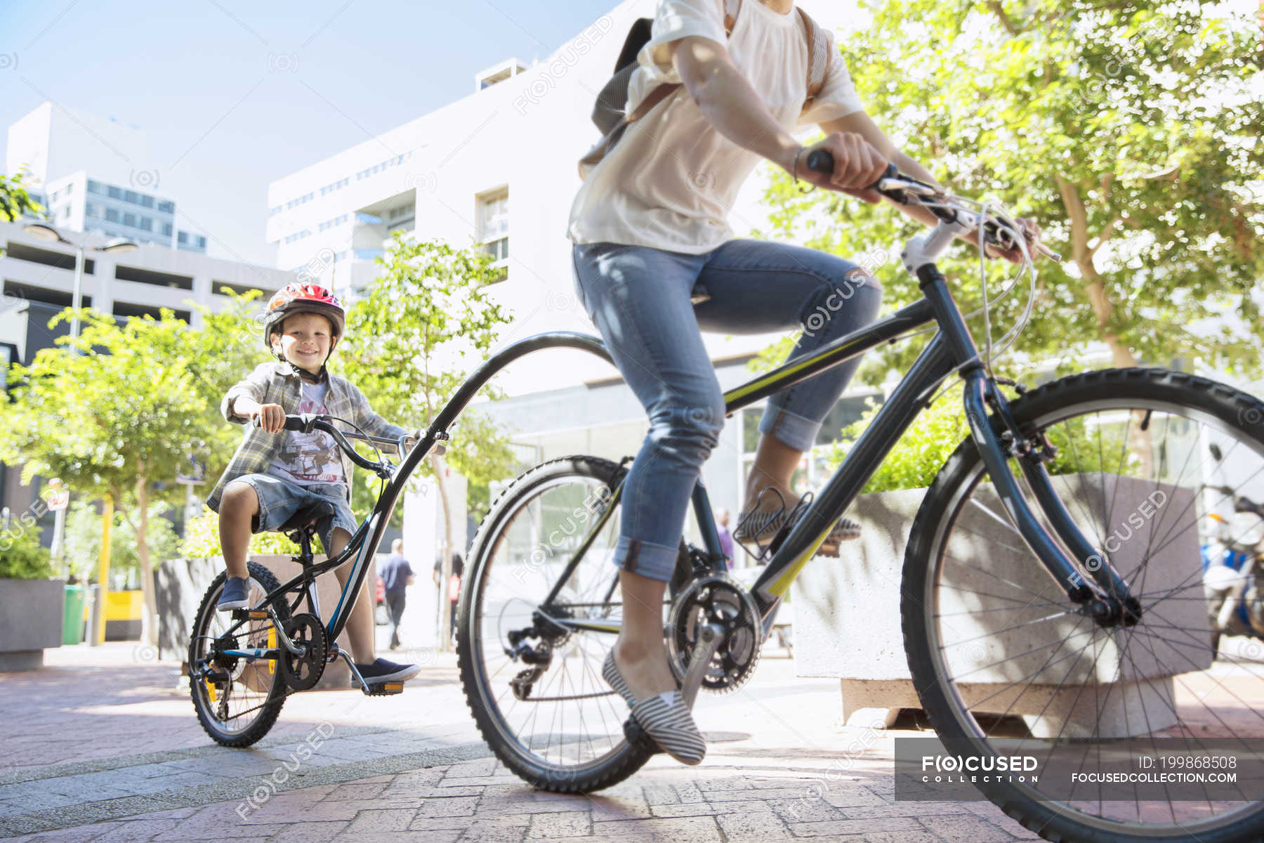 Son in helmet riding tandem bicycle with mother in urban park — mode of