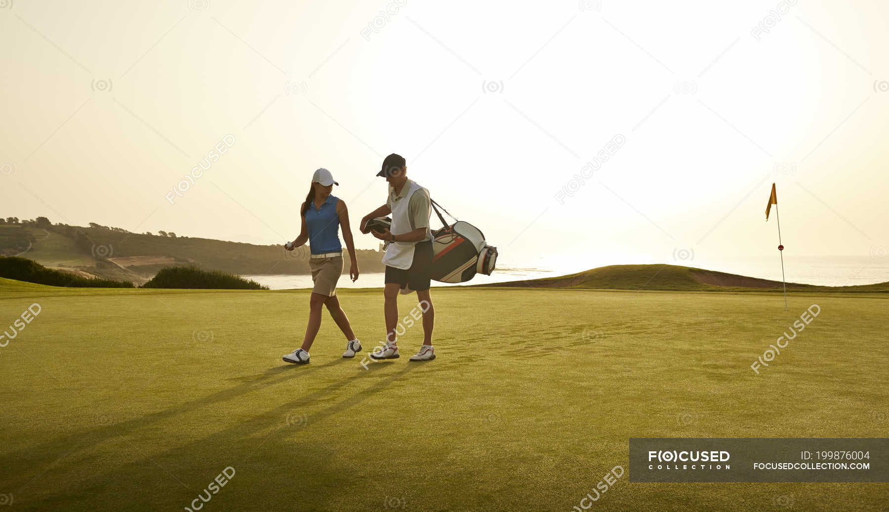 Caddy and woman walking on golf course overlooking ocean — Full Length, golfers Stock Photo
