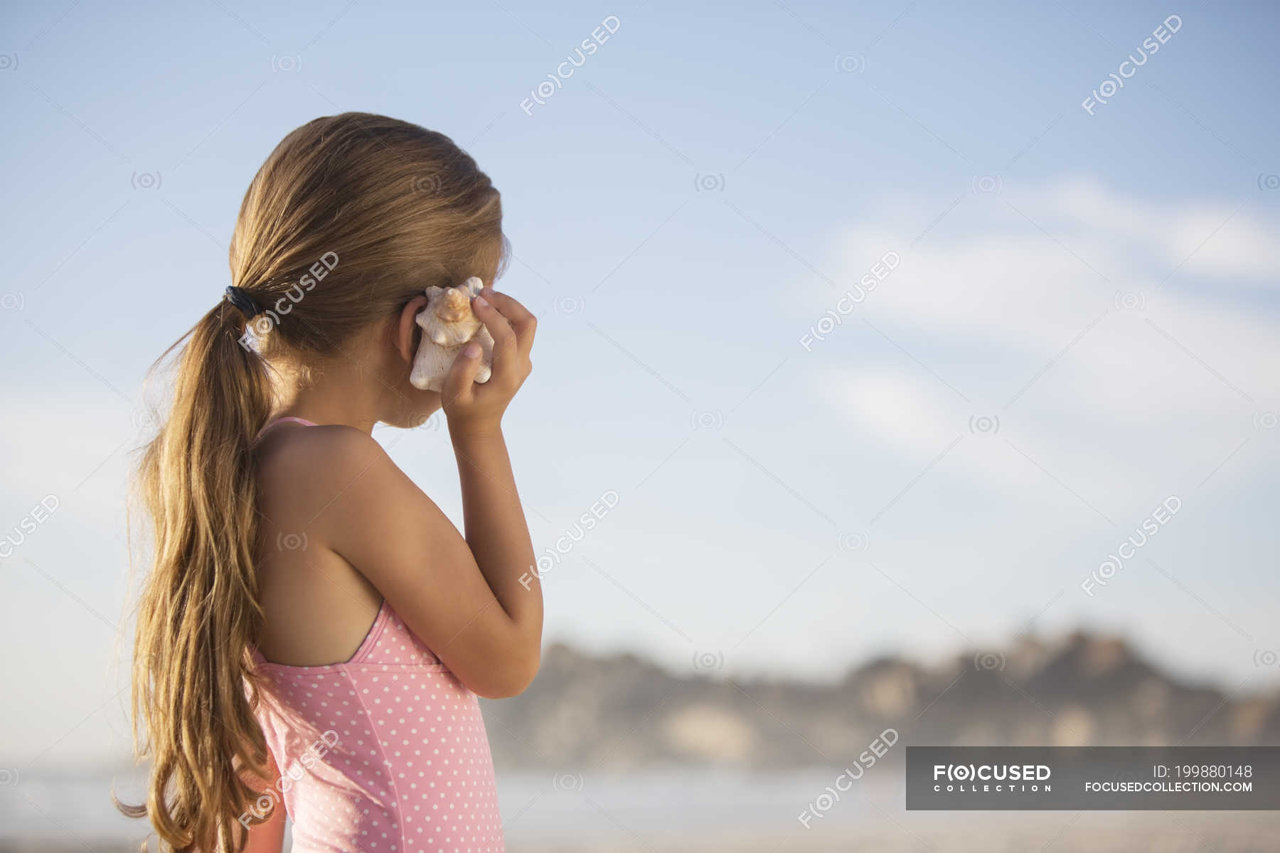 Girl listening to seashell on beach — innocence, curiosity Stock