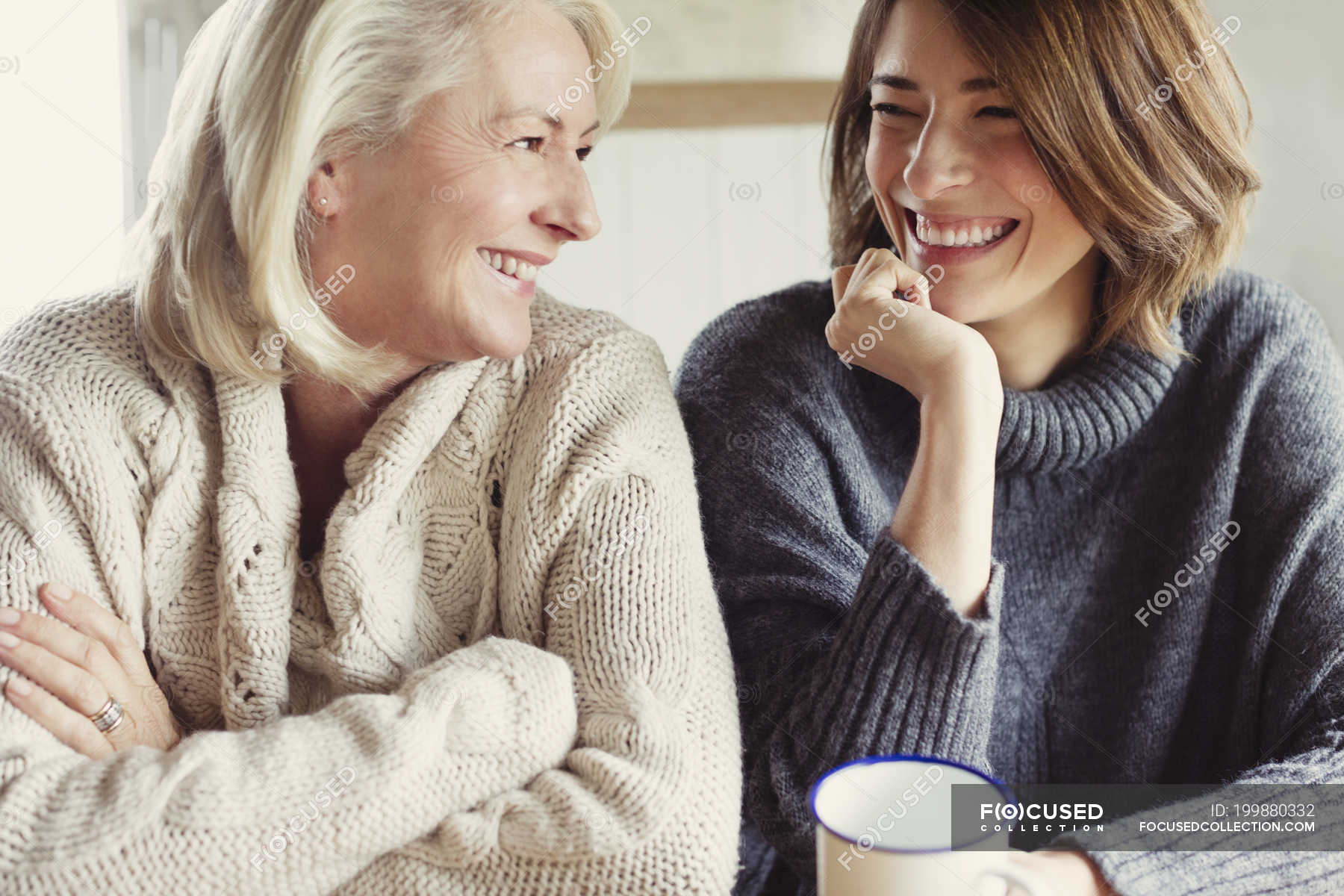 Laughing mother and daughter in sweaters drinking coffee — Hand On Chin ...