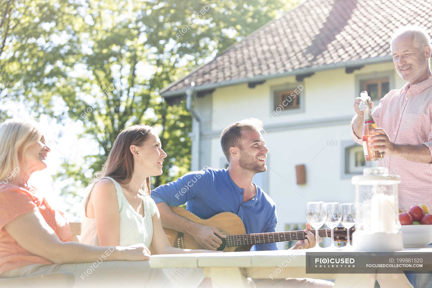 Father Opening Bottle Of Rose Wine For Family At Sunny Patio Table