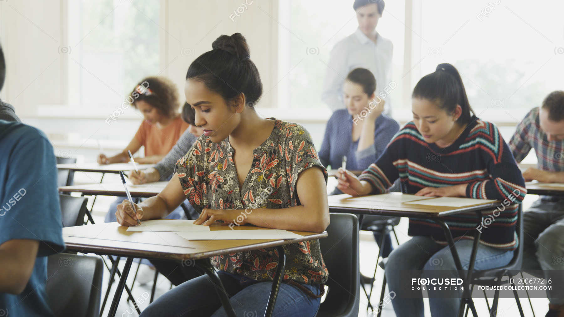 College Students Taking Test At Desks In Classroom Selective