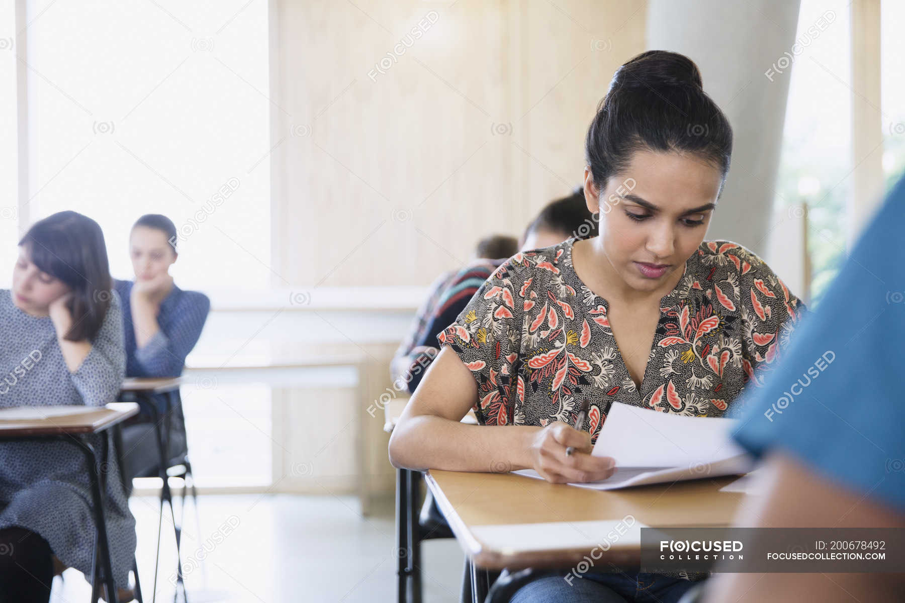 Serious Female College Student Taking Test At Desk In Classroom