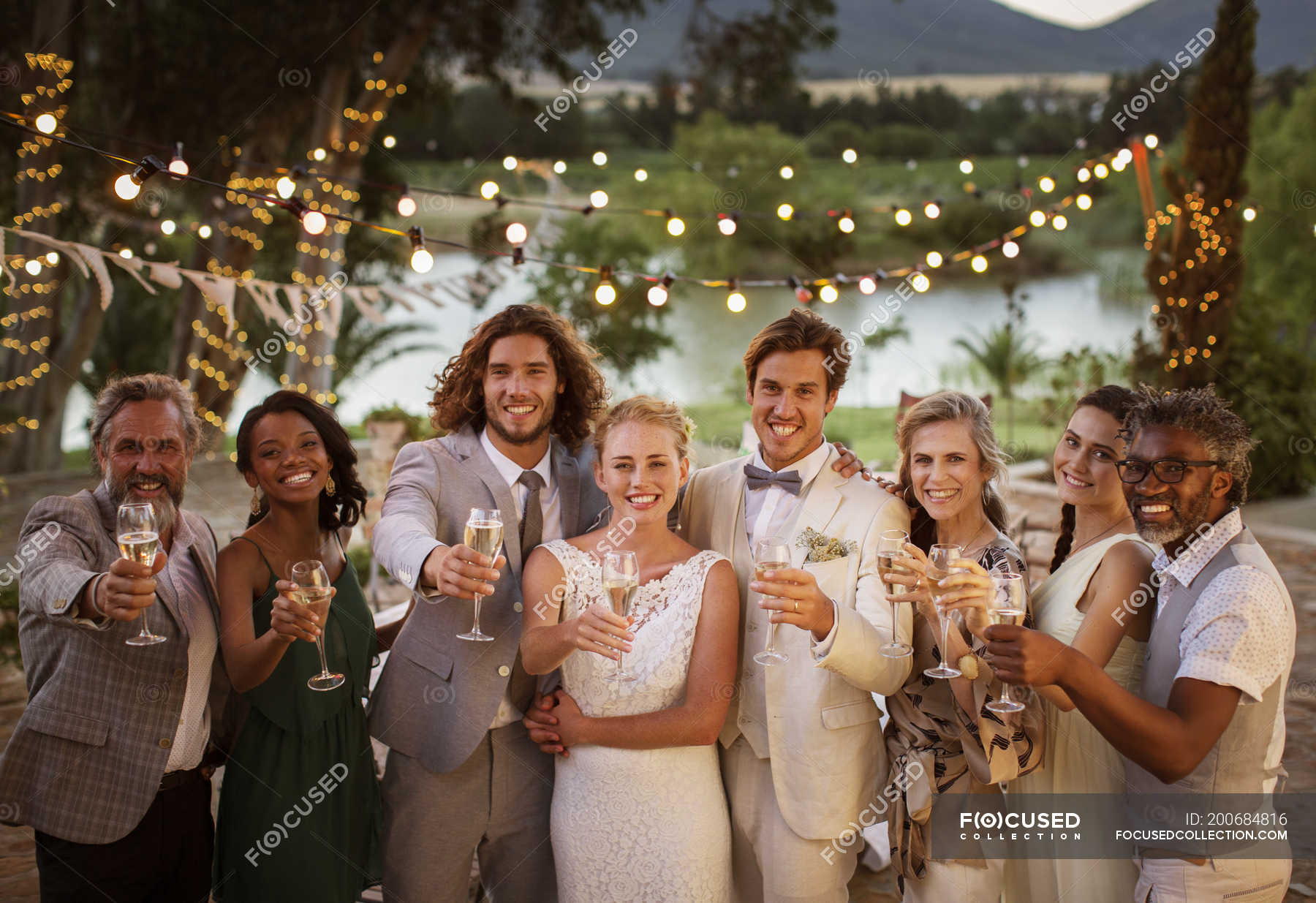 Portrait Of Young Couple With Guests Toasting With Champagne