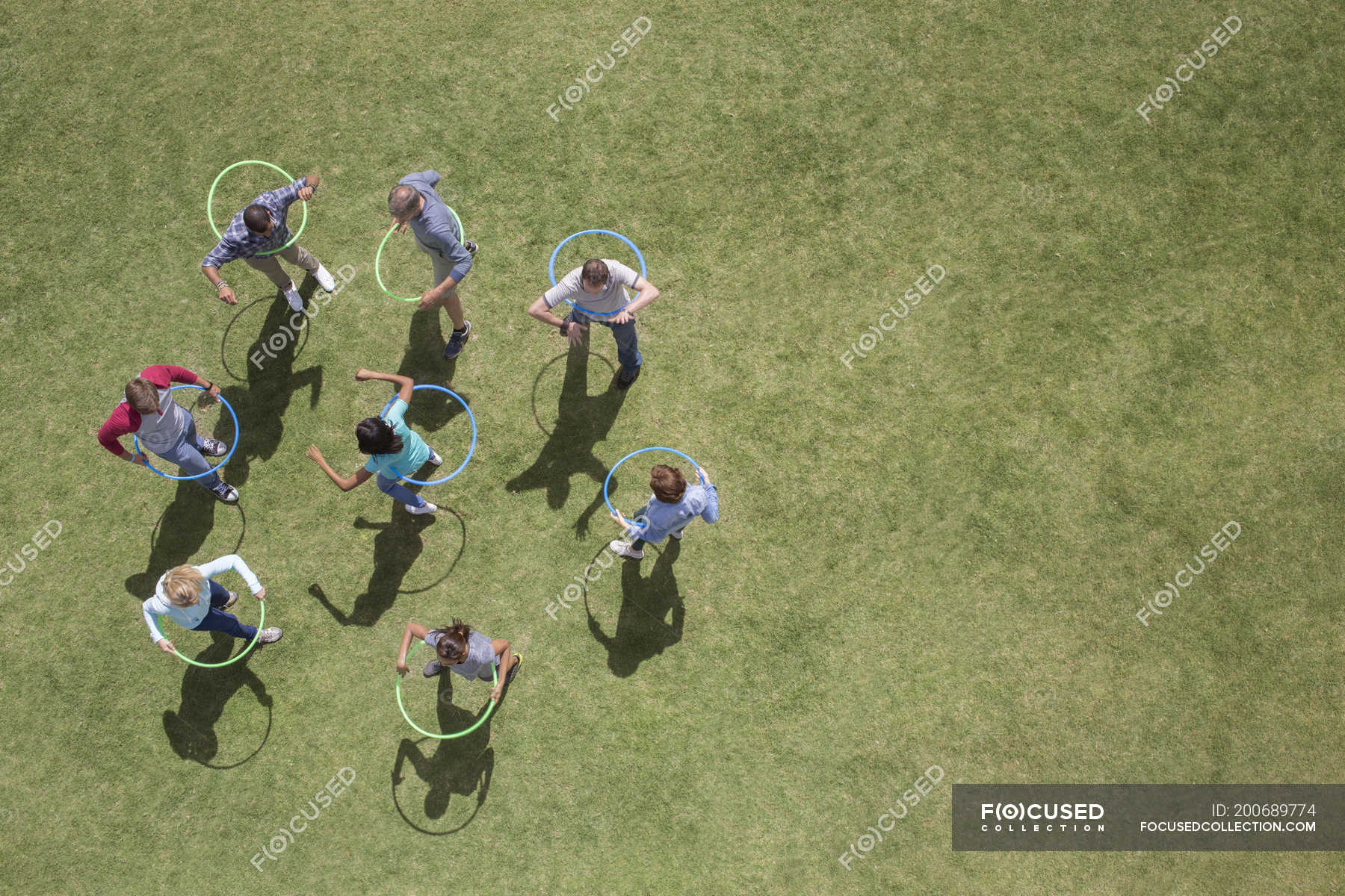 People Spinning In Plastic Hoops In Sunny Grass — High Angle View