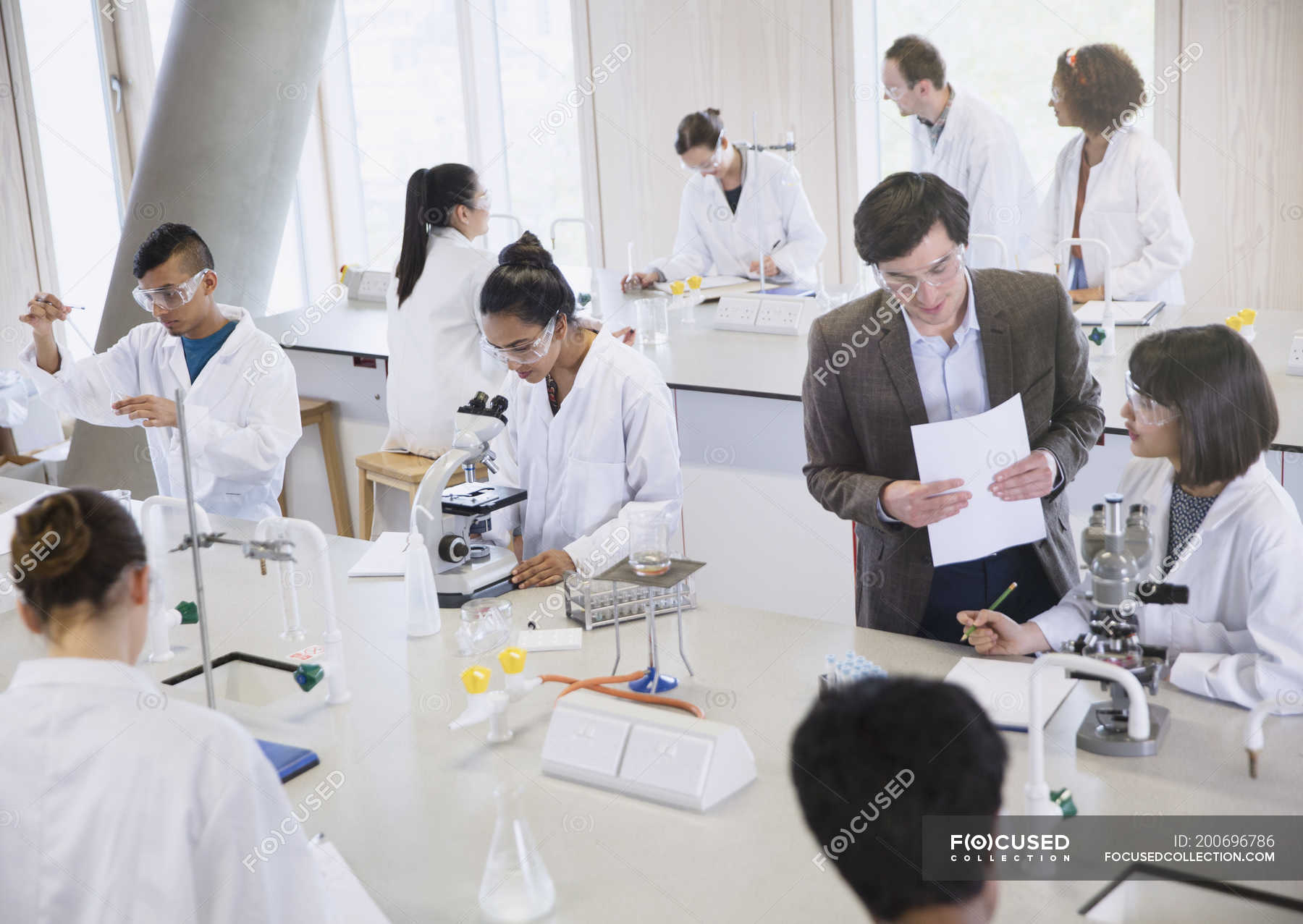Science professor and college students using microscopes in science laboratory classroom